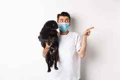 科维德动物检疫概念年轻的男人。脸面具持有可爱的黑色的哈巴狗狗宠物老板复制空间站白色背景