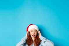 冬天假期圣诞节夏娃概念头可爱的红色头发的人女孩圣诞老人他底复制空间盯着标志站蓝色的背景