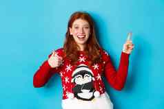 快乐圣诞节快乐的红色头发的人女孩圣诞节毛衣指出手指上角落里显示一年促销竖起大拇指批准赞美产品