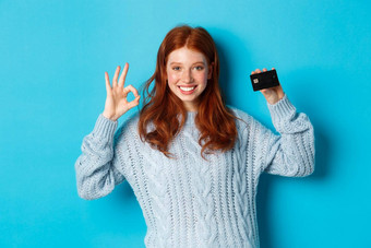快乐红色头发的人女孩毛衣显示信贷卡<strong>标志推荐</strong>银行提供站蓝色的背景