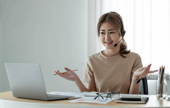 微笑亚洲女人自由职业者穿耳机沟通客户端视频电脑调用千禧愉快的专业女导师给在线语言类