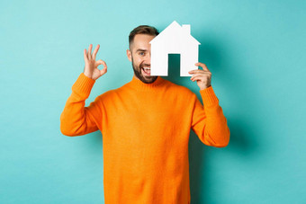 真正的房地产概念满意男人。推荐机构显示标志房子模型站蓝色的背景