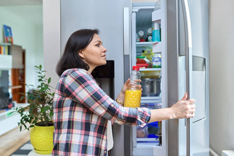 女人打开冰箱首页厨房持有瓶橙色汁