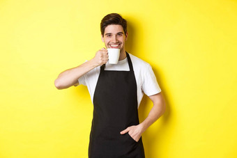 咖啡馆咖啡师喝杯咖啡微笑穿黑色的围裙站黄色的背景