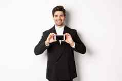 肖像有吸引力的商人黑色的西装持有智能手机水平显示屏幕微笑很高兴站白色背景