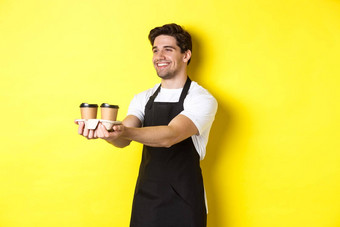 友好的咖啡师黑色的围裙给外卖订单持有杯咖啡微笑站黄色的背景