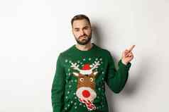 冬天假期圣诞节不高兴脾气暴躁的的家伙抱怨穿有趣的毛衣指出手指上角落里促销白色背景