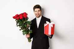 概念假期的关系庆祝活动英俊的自信男人。黑色的西装日期持有花束玫瑰现在站白色背景