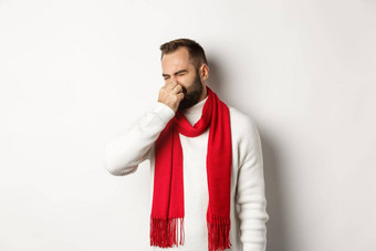 不高兴的家伙关闭鼻子坏气味扮鬼脸恶心站白色背景白色毛衣红色的围巾