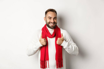 冬天假期购物概念快乐的有胡子的男人。红色的圣诞节围巾显示拇指批准推荐商店站白色背景