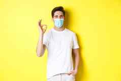 概念冠状病毒流感大流行社会距离自信年轻的男人。医疗面具显示标志眨眼黄色的背景