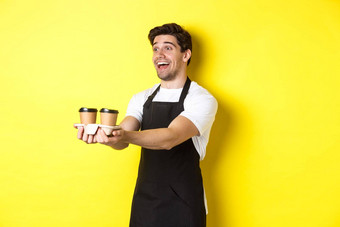友好的咖啡师黑色的围裙给外卖订单持有杯咖啡微笑站黄色的背景