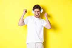 快乐男人。跳舞听音乐白色耳机站黄色的背景