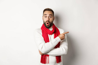 圣诞节假期庆祝活动概念惊讶有胡子的男人。指出手指深刻的印象相机站红色的围巾毛衣白色背景