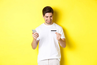 的家伙使在线订单注册信贷卡移动应用程序持有智能手机微笑站黄色的背景