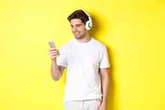 英俊的现代的家伙选择播放列表智能手机穿耳机站黄色的背景
