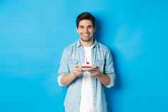 微笑男人。庆祝生日持有生日蛋糕蜡烛站蓝色的背景