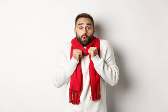 圣诞节假期庆祝活动概念男人。敬畏相机站惊讶感觉冷一年穿红色的围巾毛衣白色背景