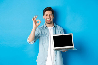 年轻的男人。显示移动PC屏幕标志批准促销互联网微笑满意站蓝色的背景