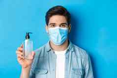 概念冠状病毒流感大流行预防措施特写镜头年轻的男人。医疗面具建议手洗手液显示防腐剂瓶站蓝色的背景