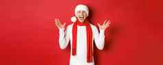 肖像快乐惊讶英俊的男人。庆祝一年祝快乐圣诞节穿圣诞老人他围巾告诉大新闻站红色的背景