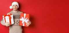 图像快乐的有吸引力的的家伙持有圣诞节礼物站圣诞老人他冬天毛衣微笑快乐站红色的背景