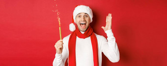 概念圣诞节冬天假期庆祝活动英俊的男人。庆祝一年有趣的持有炯炯有神的眼睛微笑穿圣诞老人他站红色的背景