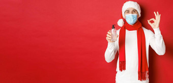 概念科维德圣诞节假期流感大流行有吸引力的男人。圣诞老人他医疗面具显示<strong>标志推荐</strong>手洗手液站红色的背景