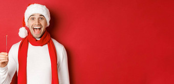概念圣诞节冬天假期庆祝活动特写镜头快乐英俊的男人。圣诞老人他围巾有趣的一年聚会，派对持有炯炯有神的眼睛微笑红色的背景