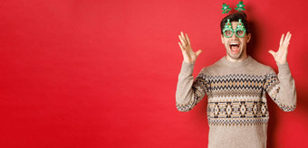 图像兴奋惊讶高加索人的家伙聚会，派对眼镜圣诞节毛衣提高手使大公告享受一年庆祝活动红色的背景