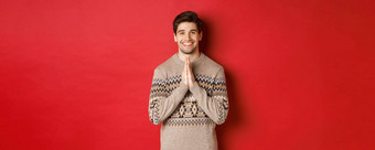 图像快乐可爱的男人。圣诞节毛衣支持持有手微笑感觉感激的站红色的背景
