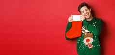 肖像快乐有吸引力的男人。绿色毛衣很高兴收到礼物圣诞节长袜站红色的背景