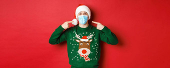概念一年冠状病毒社会距离快乐男人。圣诞老人他圣诞节毛衣推荐穿医疗面具聚会，派对站红色的背景