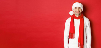 快乐高加索人的家伙庆祝圣诞节微笑穿圣诞老人他围巾白色毛衣享受一年假期站红色的背景