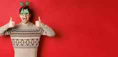 图像兴奋英俊的的家伙聚会，派对眼镜圣诞节毛衣显示竖起大拇指赞扬伟大的一年庆祝活动站红色的背景