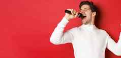英俊的的家伙白色毛衣唱歌首歌持有麦克风执行卡拉ok酒吧站红色的背景