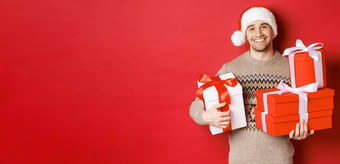 概念冬天假期一年庆祝活动肖像可爱的微笑男人。准备礼物圣诞节持有礼物相机感人的红色的背景