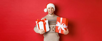 概念冬天假期一年庆祝活动肖像自信厚颜无耻的年轻的男人。准备礼物圣诞节眨眼持有礼物站红色的背景
