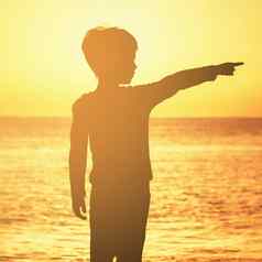 轮廓男孩拇指提高了日出日落海滨海洋橙色天空橙色海海洋男孩显示指数手指一边