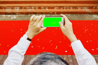 男人的手拍摄电话空绿色屏幕红色的地毯