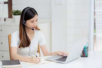 年轻的亚洲女人穿耳机研究在线电子学习桌子上女孩穿耳机学习互联网移动PC电脑首页正常的距离<strong>教育培训</strong>