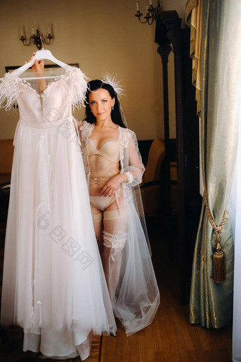 新娘穿着闺房透明的衣服内衣持有婚礼衣服手室内房子