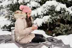美丽的女人温暖的冬天衣服持有杯喝热茶咖啡在户外雪一天
