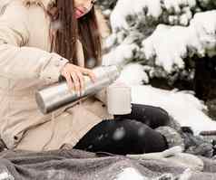 美丽的女人温暖的冬天衣服持有热水瓶喝热茶咖啡在户外雪一天