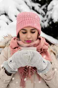 美丽的女人温暖的冬天衣服持有杯喝热茶咖啡在户外雪一天