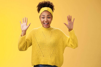迷人的兴奋微笑友好的千禧非裔美国人女孩提高手隐藏显示手掌高投降站逗乐激动咧着嘴笑有趣的摆姿势黄色的背景