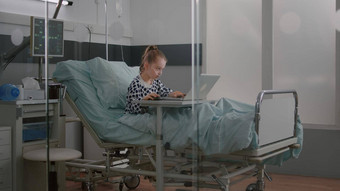 <strong>住院</strong>生病的女孩穿氧气鼻管坐着床上玩在线电子游戏移动PC