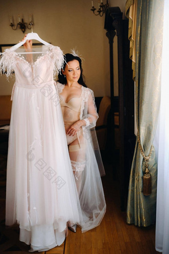 新娘穿着闺房透明的衣服内衣持有婚礼衣服手室内房子