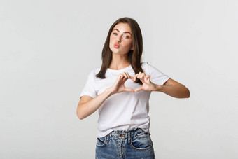 可爱的浅黑肤色的女人女孩撅嘴吻显示心手势