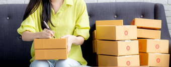 年轻的亚洲女人写作地址包裹盒子首页交付订单客户航运物流商人在线卖方业务老板锻造在线购物电子商务